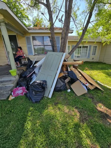 Before junk removal in Lubbock showing piles of debris, trash bags, wood, and bulky items outside a residential home